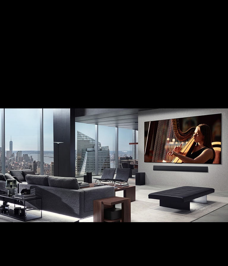 סלון עם מסך TV‏ LG True Wireless ו מקרן הקול LG Soundbar מותקנים על הקיר. תיבת ה-Zero Connect Box נראית בקושי כשהיא ממוקמת מתחת לשולחן צדדי ליד הספה, מה שמראה כיצד ניתן למקם אותה בקלות בכל מקום. הסלון כולו נראה מסודר ונקי.