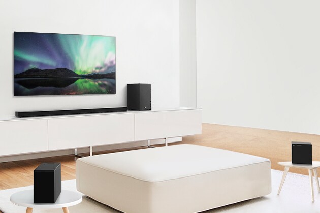 טלוויזיה וסאונד-בר בסלון לבן עם ספה לבנה במרכז. רמקולים ממוקמים בשתי קצוות הספה.