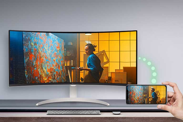 יש מסך המונח על השולחן, ומימין, טלפון המציג את אותו המסך כאשר המסך גלוי.