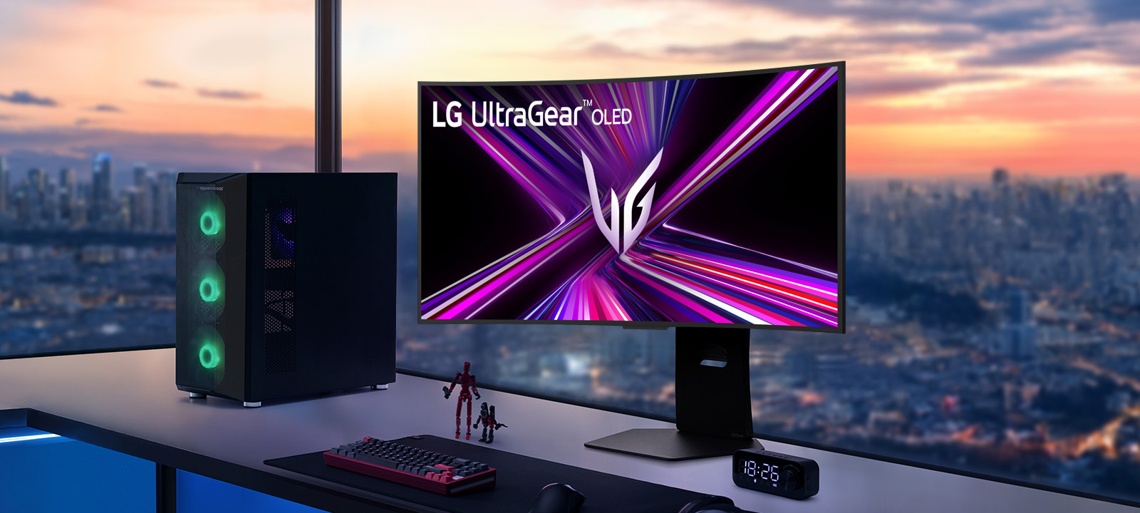 צג LG UltraGear OLED על שולחן גיימינג עם מערכת מחשב, המשקיף על נוף עירוני בשעת השקיעה.