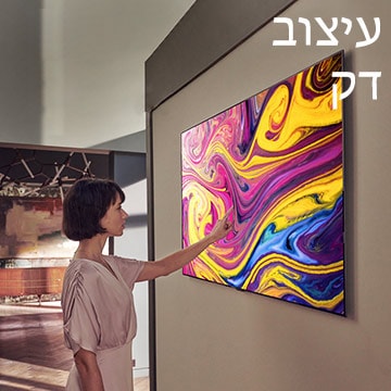 אישה מביטה על טלוויזיה התלויה על הקיר ומציגה יצירת אומנות.