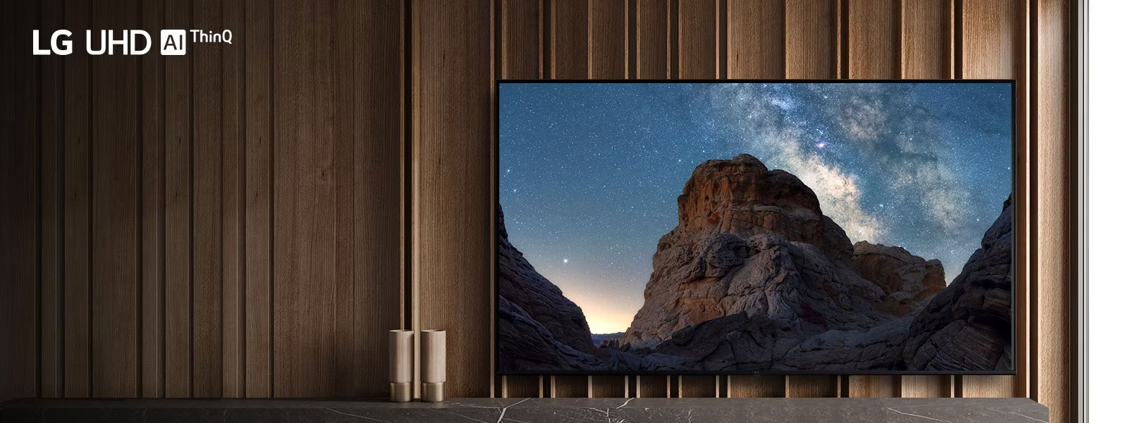 טלוויזיה ניצבת בחדר יוקרתי ורחב ידיים ובמסך מוצגת תמונת טבע של שמי לילה זרועי כוכבים והרים סלעיים.