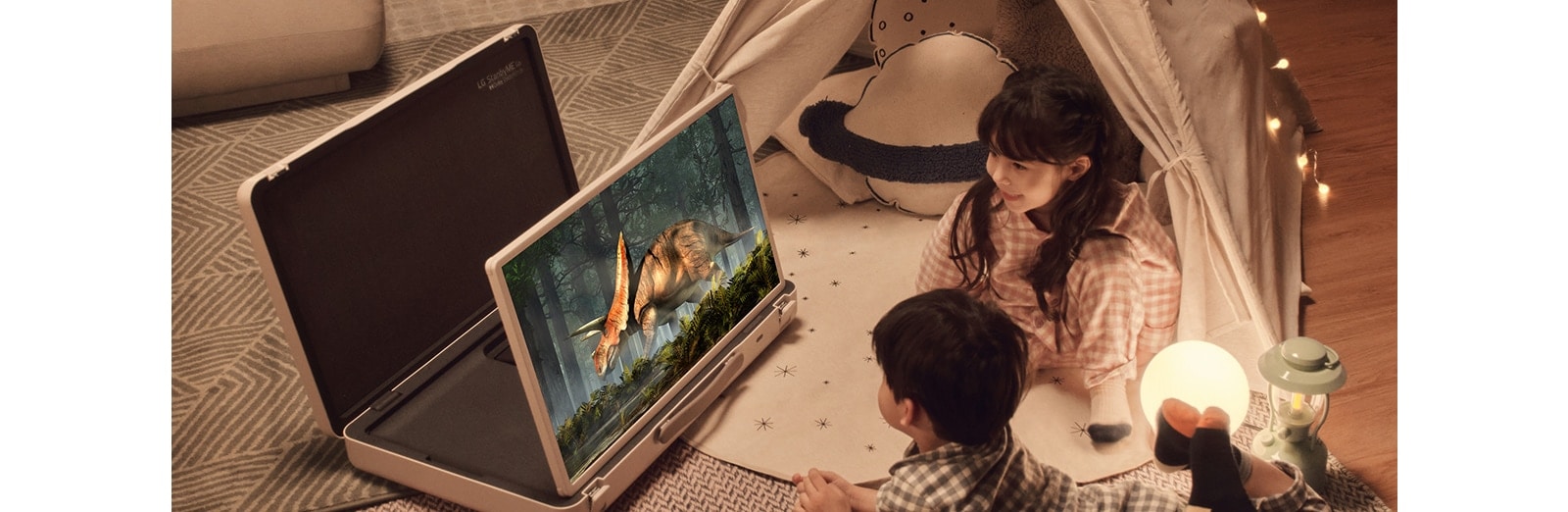 כיסוי ה-LG StanbyME Go נפתח והמסך מורם. שני ילדים בבית בקמפינג עם אוהל ותאורה חמה ונעימה. הם צופים בווידאו על מסך ה-StanbyME Go.