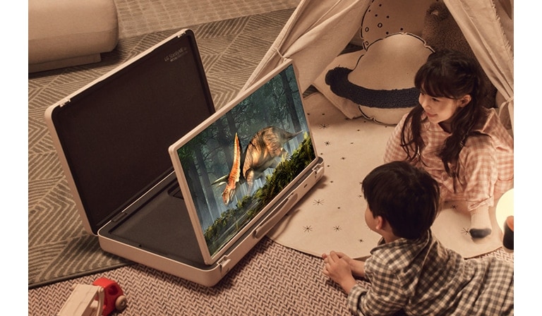 כיסוי ה-LG StanbyME Go נפתח והמסך מורם. שני ילדים בבית בקמפינג עם אוהל ותאורה חמה ונעימה. הם צופים בווידאו על מסך ה-StanbyME Go.