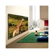 LG טלוויזיה חכמה LG QNED evo AI Mini LED QNED85 4K 2026 86 אינץ, העיצוב של טלוויזיית LG QNED evo AI QNED85 Mini LED Ultra Big TV מותקן על הקיר בחלל מגורים מואר, ומוצגת ג'ירפה בנוף טבעי עם פרטים מלאי חיים המדגישים קנה מידה ונוכחות סוחפים עבור ילד היושב בקרבת מקום., 86QNED85B6T, thumbnail 14