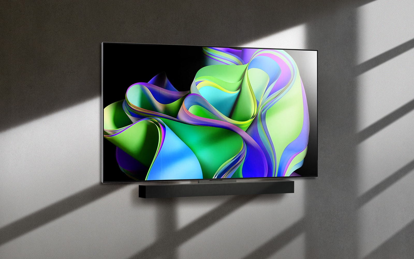 A video opens with the words LG OLED evo against a black background. The words enlargen and fill with color. Then the scene transitions to LG OLED C3, showing a colorful abstract artwork with a Soundbar against a white background. The white background becomes a wall in a room to which the TV attaches. 