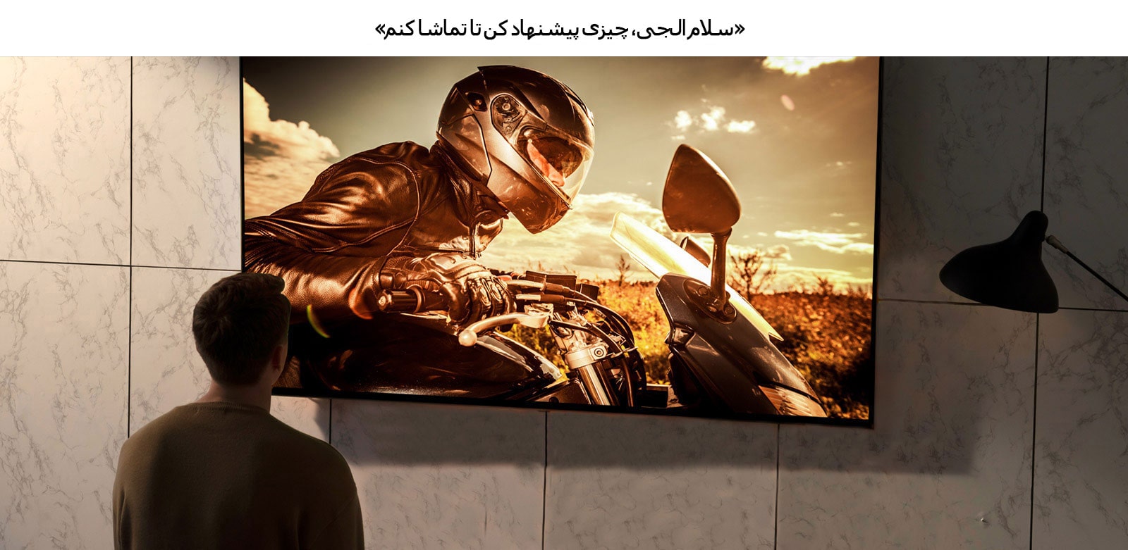 نمای پشت از مردی که در حال تماشای تلویزیونی است که روی دیوار اتاق پذیرایی نصب است. صحنه‌ای از فیلم موتورسیکلتی روی صفحه نمایش داده می‌شود.