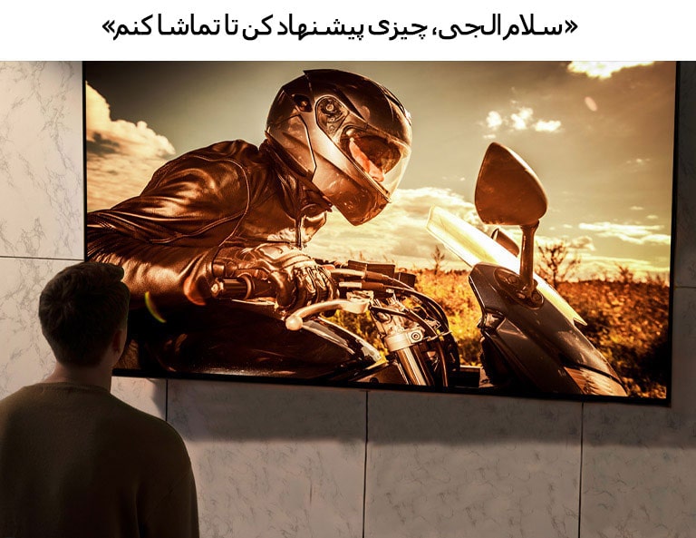 نمای پشت از مردی که در حال تماشای تلویزیونی است که روی دیوار اتاق پذیرایی نصب است. صحنه‌ای از فیلم موتورسیکلتی روی صفحه نمایش داده می‌شود.