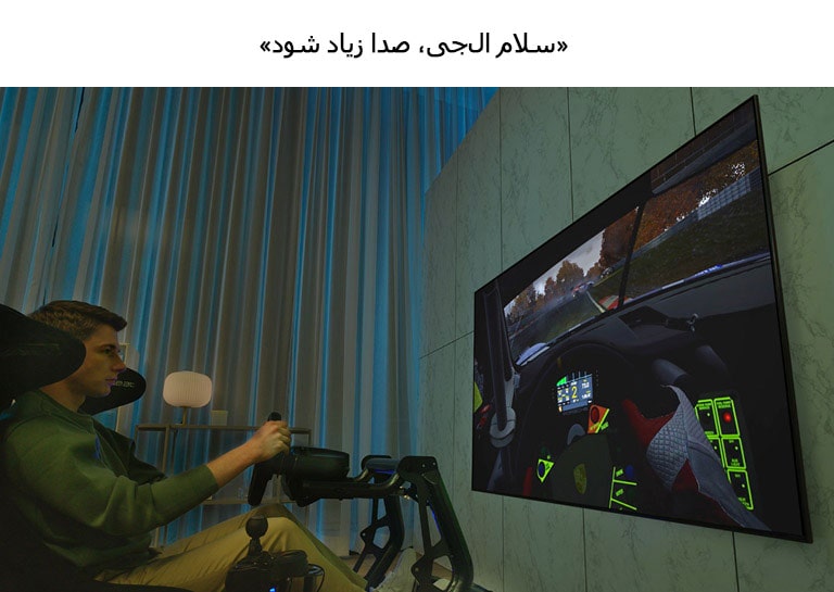 مردی که روی صندلی مسابقه جلوی تلویزیون بزرگی نشسته و ماشین‌سواری بازی می‌کند.