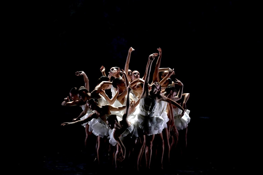 Un gruppo di ballerine in tutù bianchi posano per formare insieme un fiore.