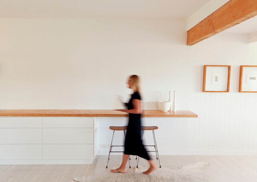 Donna che cammina lungo un tavolo penisola minimalista e sgabelli alti da cucina.