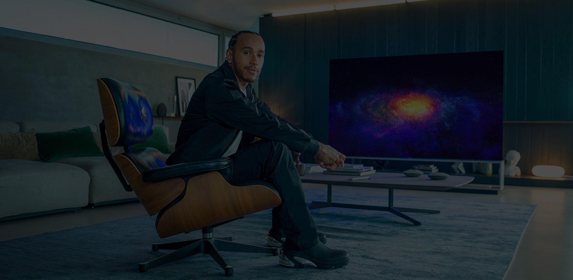 Lewis Hamilton che siede in poltrona e, dietro di lui, la TV OLED 8K LG SIGNATURE a fare da sfondo.