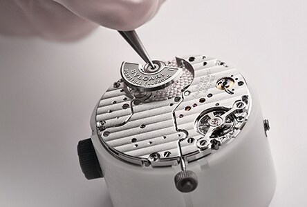 Primo piano di un artigiano che manipola un componente di un orologio.