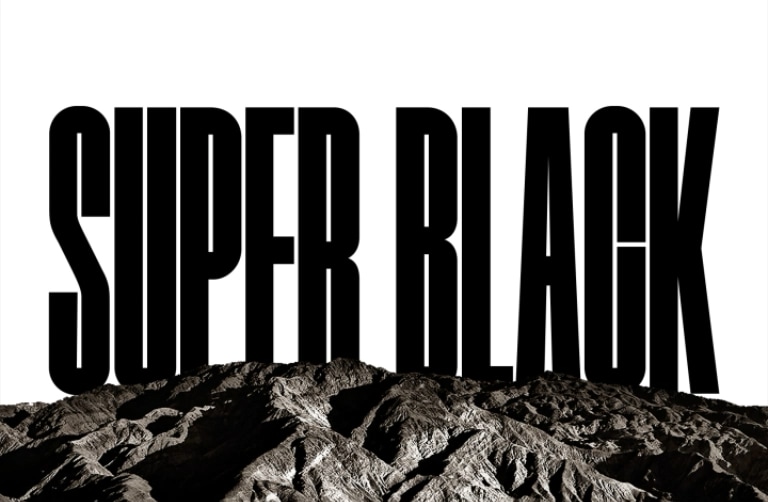  تظهر كلمتي "SUPER BLACK" (أي أسود فائق) بأحرف كبيرة باللون الأسود الغامق. يتم عرض مشهد لمنطقة جبلية سوداء عالية الوضوح ثم يرتفع المشهد ليغطي الحروف، ويكشف أيضًا عن قرية وكثبان رملية. تختفي النسخة السوداء خلف سماء سوداء.