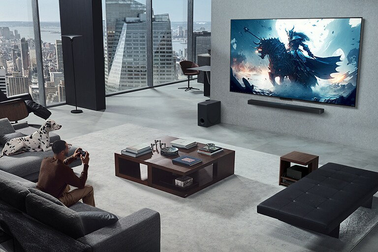 غرفة معيشة بها شخص يلعب لعبة فيديو على تلفزيون LG True Wireless TV المثبت على الحائط ومكبر الصوت LG Soundbar. يحمل وحدة تحكم في الألعاب في يده، ولكن وحدة الألعاب غير مرئية. كما لا توجد أسلاك مرئية. يتم إخفاء Zero Connect Box بعيدًا، بالكاد يظهر تحت طاولة جانبية. 