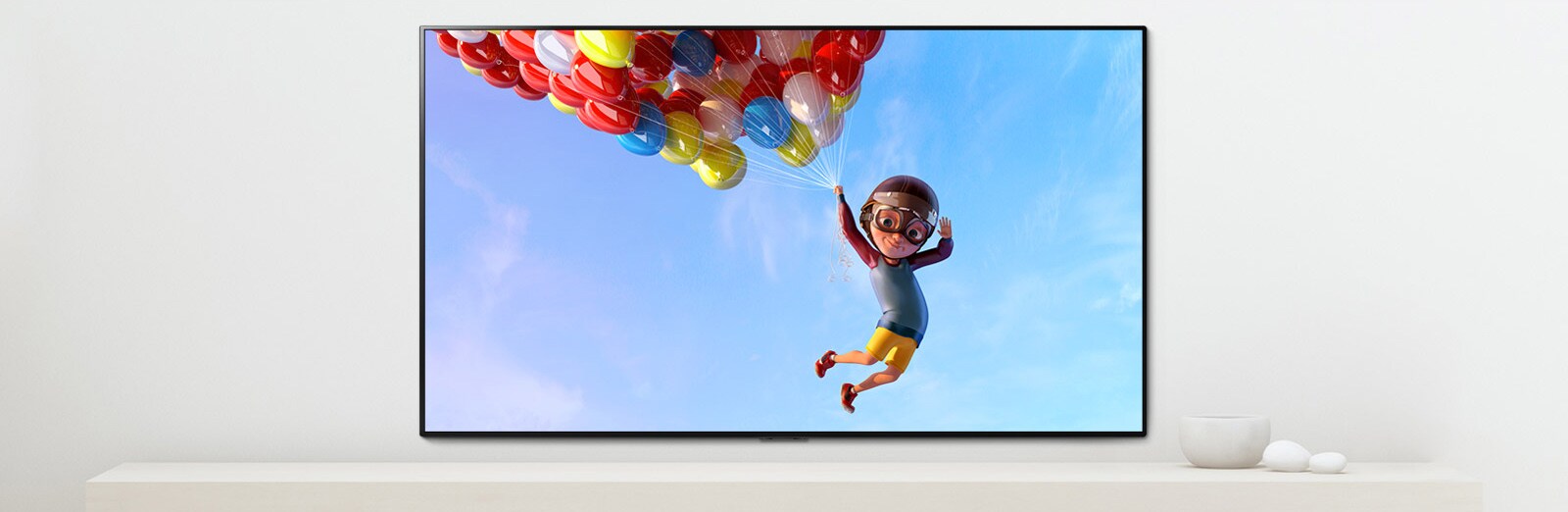 مشهد لفيلم رسوم متحركة يُظهر طفلاً معلقاً في بلالين ملونة في السماء معروضاً على شاشة تلفاز 