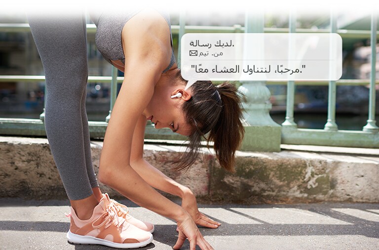 امرأة تتمدد وتنحني لتلمس الأرض بينما تستمع إلى رسالة تقرؤها سمّاعات الأذن.