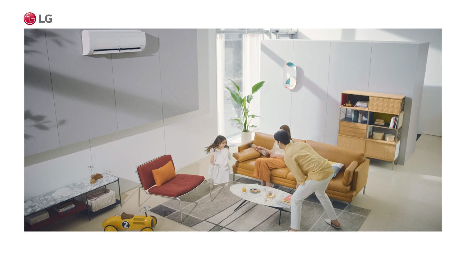 أسرة يمرح أفرادها بغرفة المعيشة مع وجود مكيف الهواء بالجزء العلوي من الصورة.