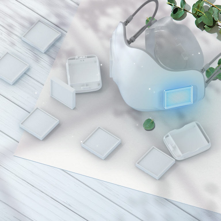 يتم عرض جهاز تنقية الهواء القابل للارتداء LG PuriCare بزاوية من الأعلى مع مرشحات HEPA من الفئة H13 منتشرة على الطاولة حوله.  يتم تمييز مكان إدخال المرشح على القناع بمربع أزرق.