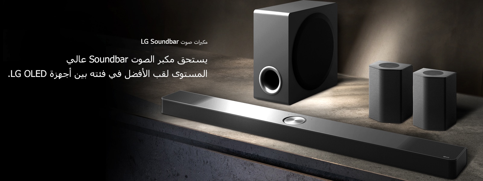 تم وضع مكبر الصوت LG Soundbar، ومكبرات الصوت الخلفية، ومضخم الصوت على رف خشبي بني في غرفة سوداء وتصويرهم بمنظور ذي زاوية في الظلام، مع تسليط ضوء على نظام الصوت فقط.