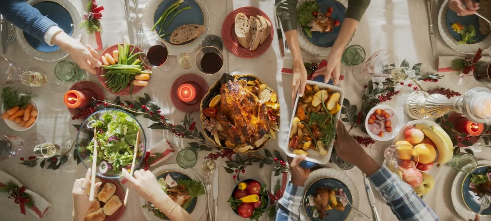 Top view of people sharing a meal with roast turkey and side dishes at a dining table.