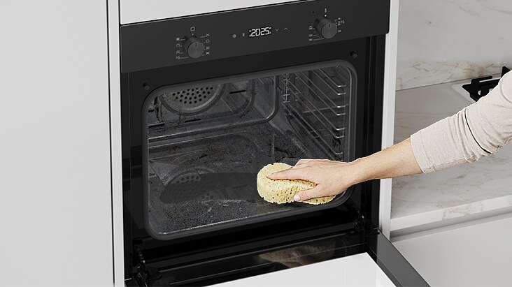 Hand cleaning the interior of a built-in oven with a sponge.