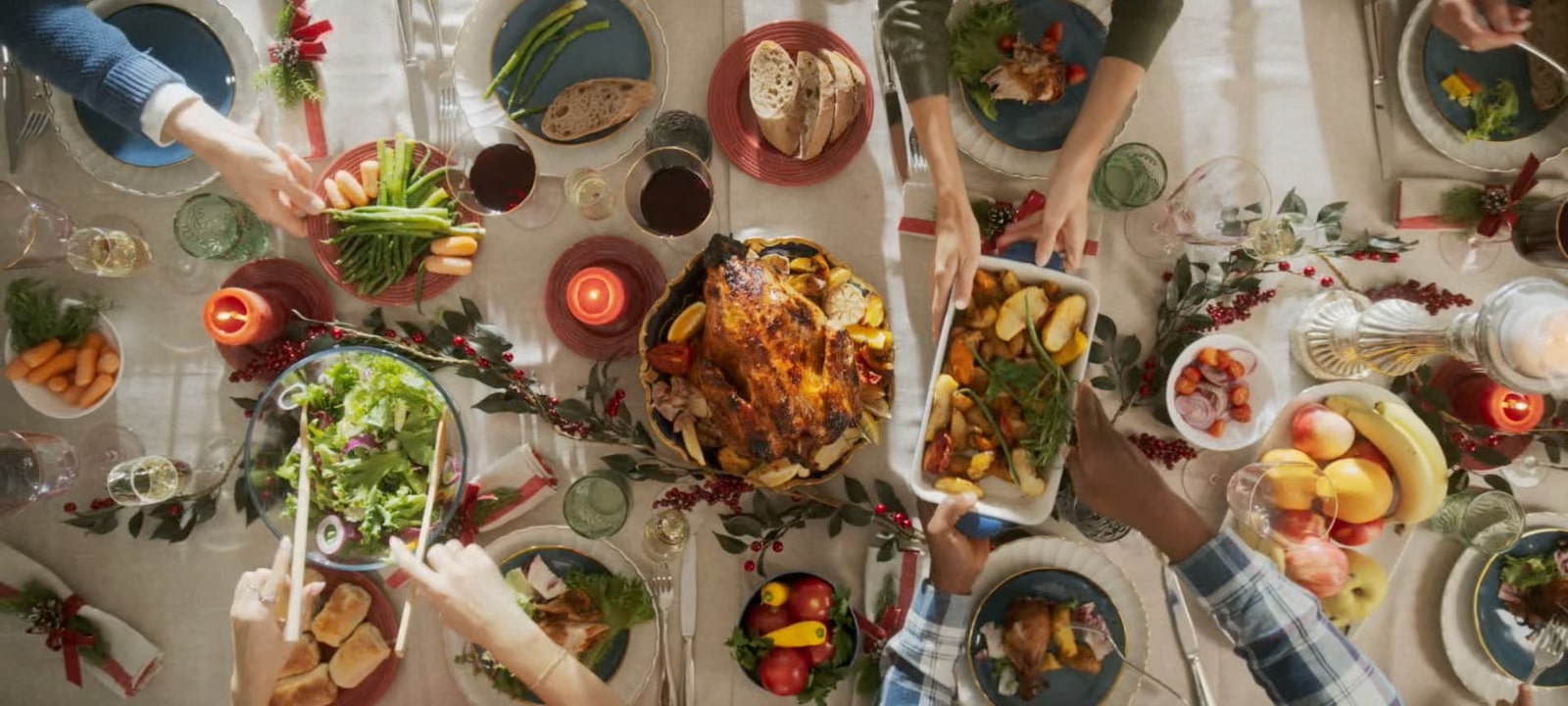 Top view of people sharing a meal with roast turkey and side dishes at a dining table.