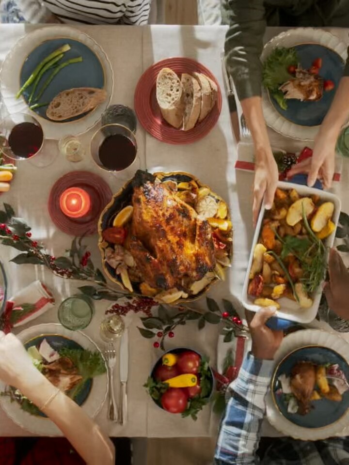 Top view of people sharing a meal with roast turkey and side dishes at a dining table.