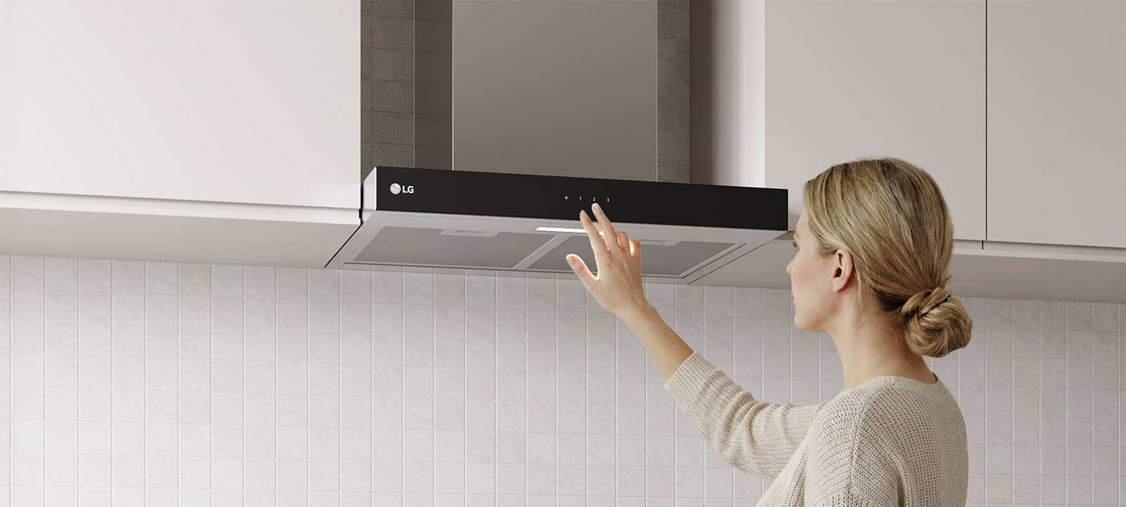 A woman adjusting the touch controls of a built-in range hood above a cooktop in a modern kitchen with a white tile wall.