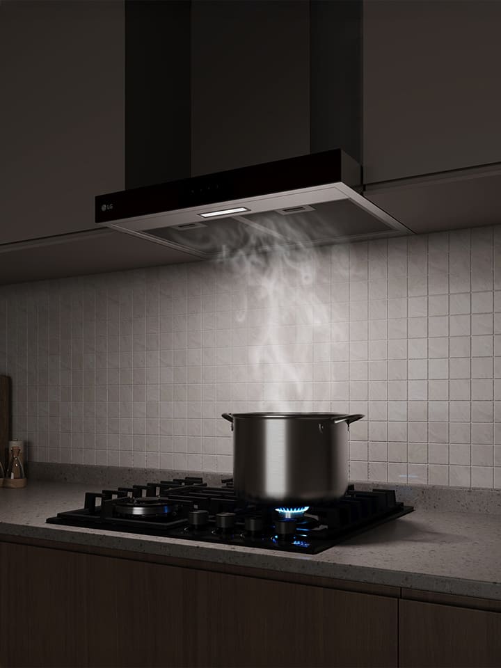 A built-in range hood above a gas cooktop draws in steam rising from a pot while cooking in a modern kitchen.