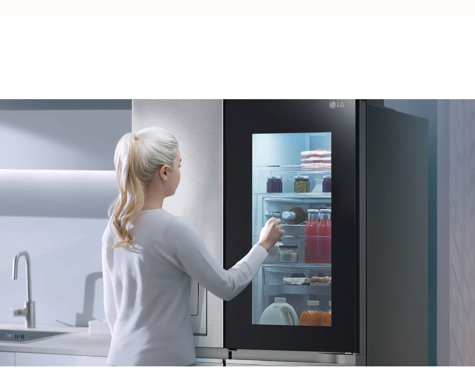 A video shows a woman approach her InstaView refrigerator and knock twice. The interior lights up and she can see the contents of her fridge without opening the door. The view zooms in to focus on the drinks in the door and then zooms out to see the woman from behind as she opens the door and grabs a drink.