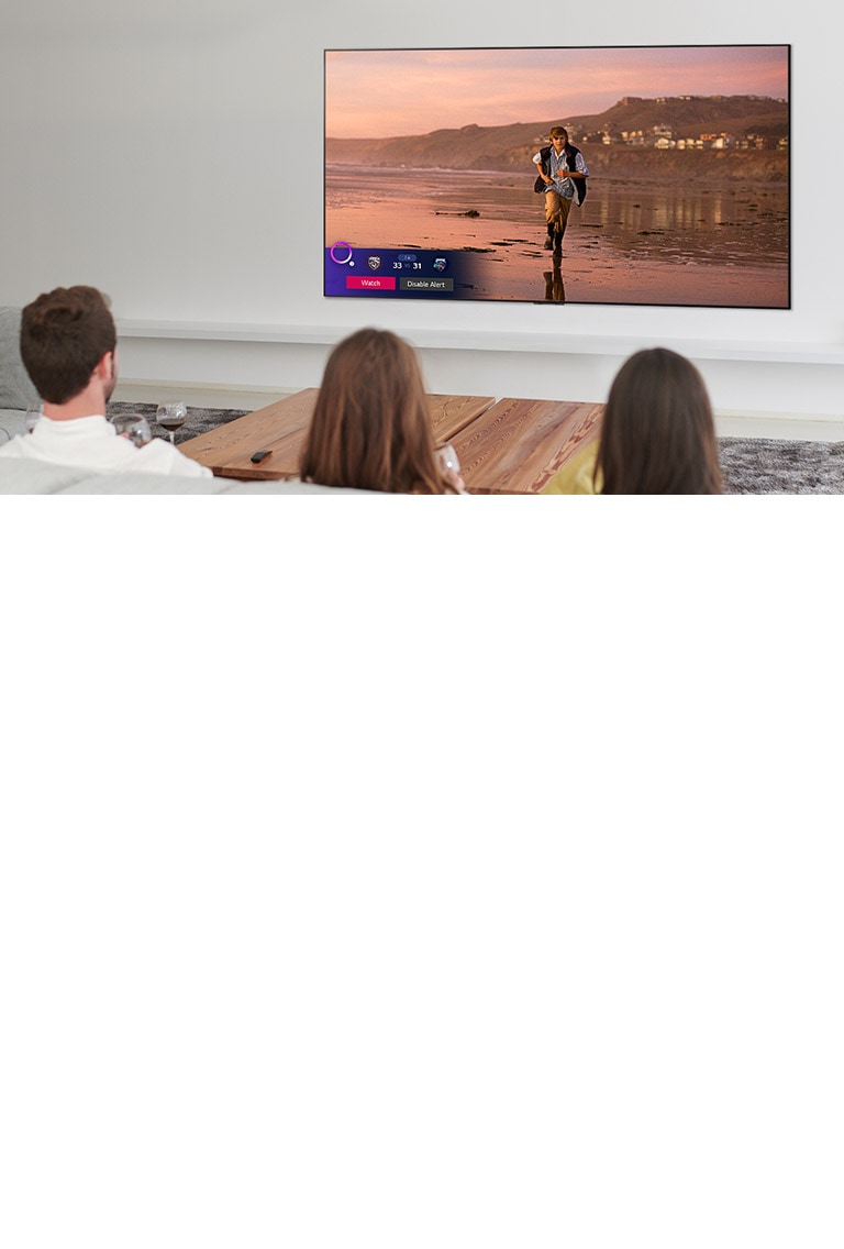 Three people watching TV screen showing a scene from a fantasy movie with a Sports Alert