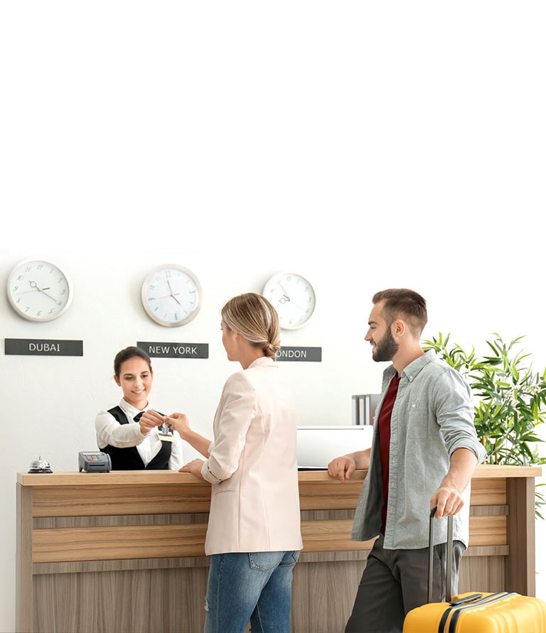 An image of a couple checking in with a receptionist at a hotel lobby.