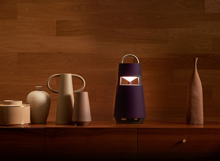 Image of the XBOOM 360 with sculptures on a shelf in a wood-toned interior background. 