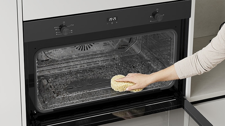 Hand cleaning the interior of a built-in oven with a sponge.
