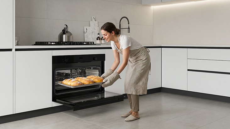 Woman placing a tray of baked pastries into a built-in oven.