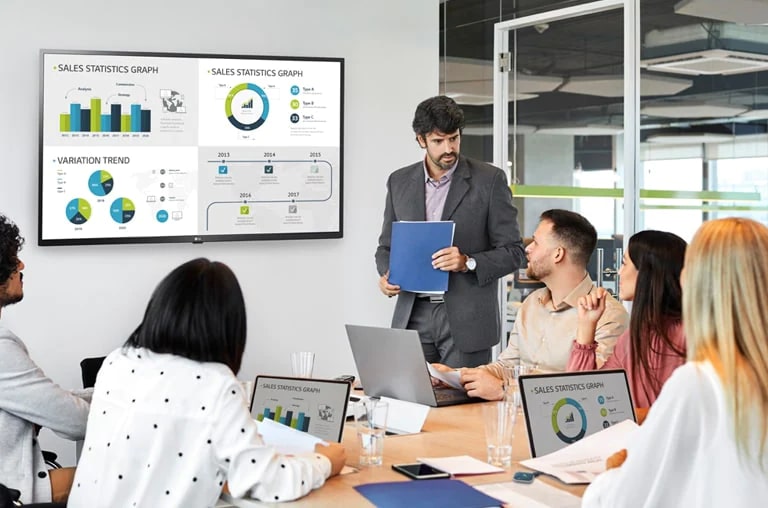 There are 6 people having a meeting and 4 PC screens are simultaneously shared on large signage hanging on the wall through the USB dongle device connected to the personal PCs.