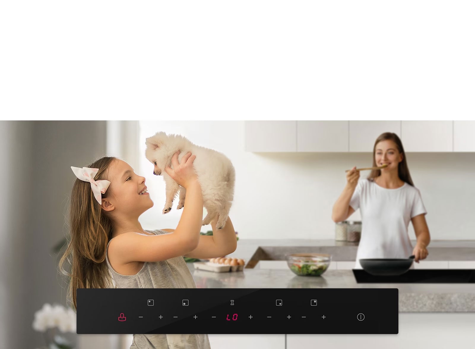 A child plays with a puppy in the foreground with a mother in the background tasting food from the cooktop. 