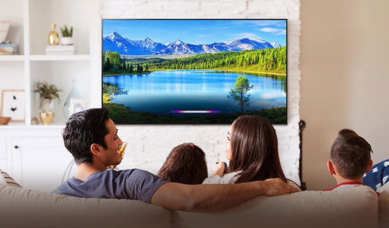 Family in bright living room looking at landscape on wall-mounted TV