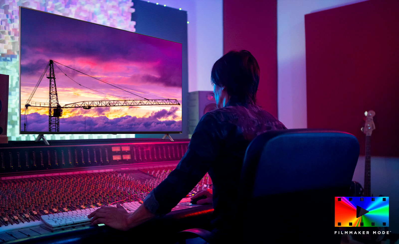 A movie director is looking at a big TV monitor, editing something. The TV screen shows a tower crane in purple sky. FILMMAKER Mode logo is placed on bottom right corner.