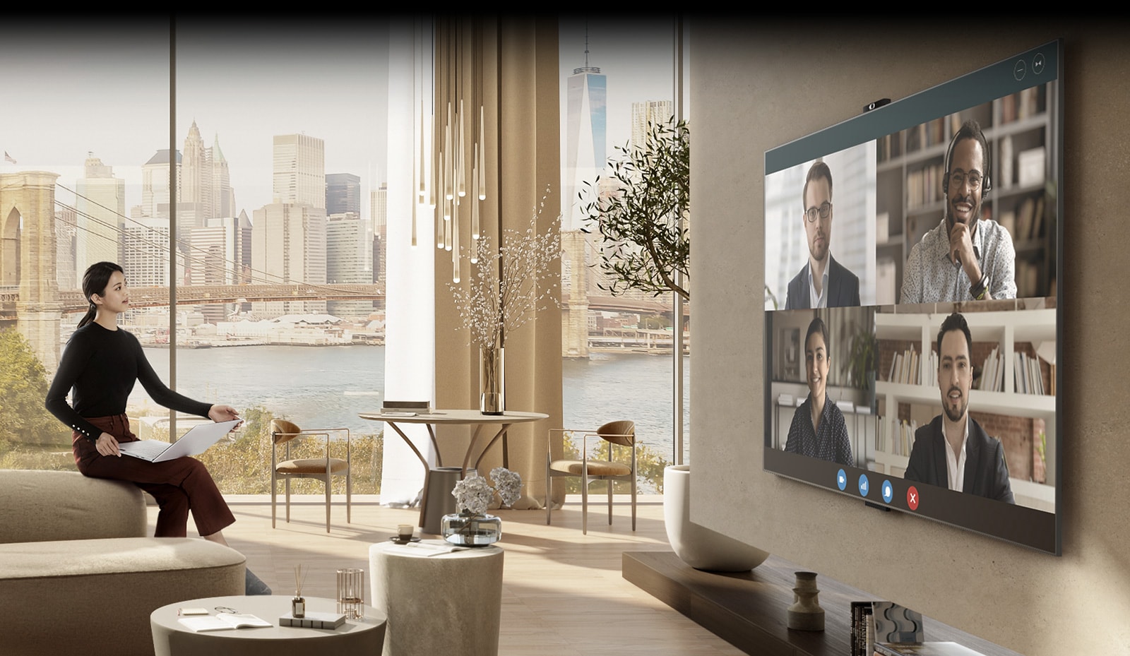 A woman is sitting on a luxurious sofa in a spacious living room. She is holding a laptop while facing a large screen on the opposite wall, indicating that she is in a video conference.