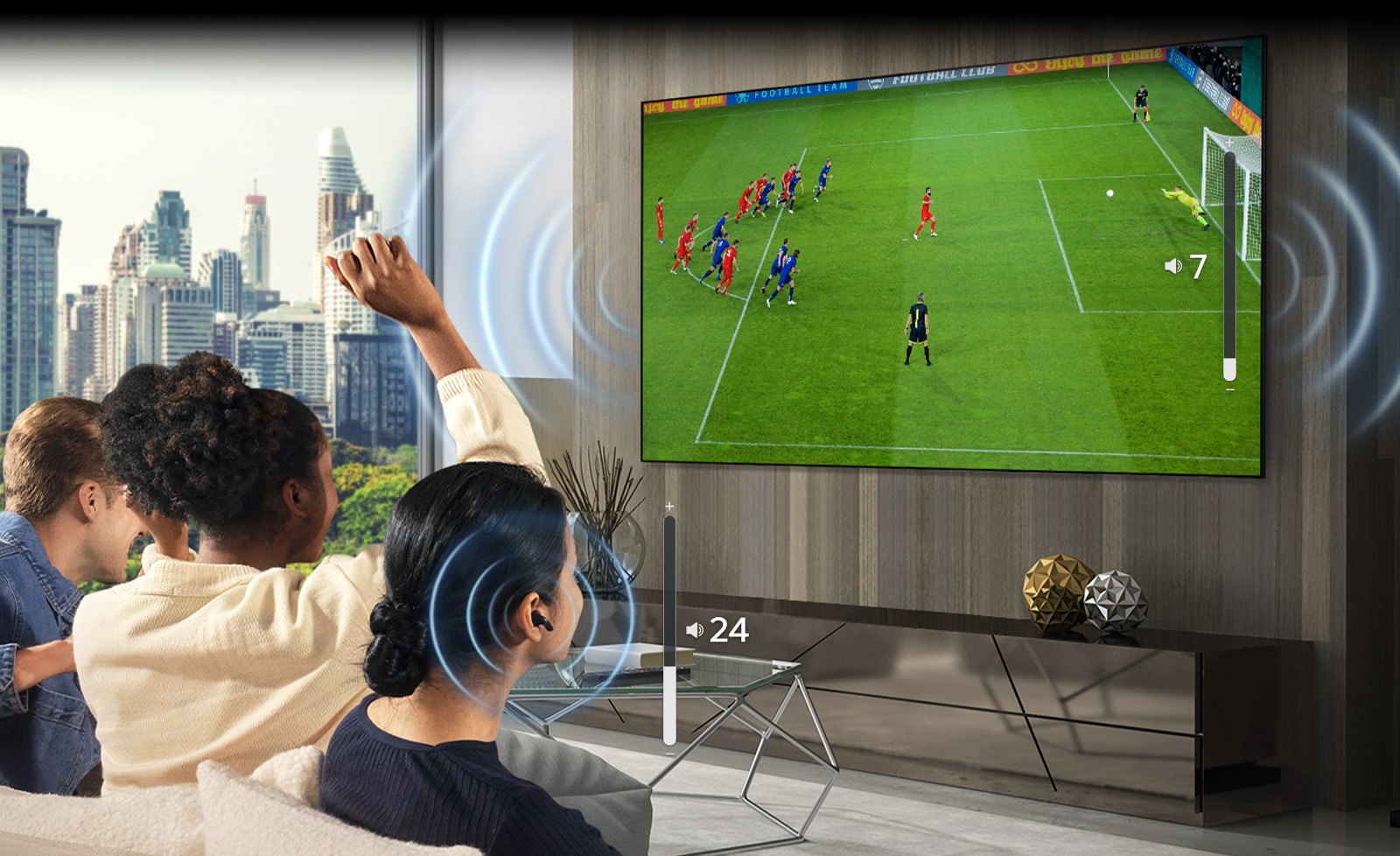 A group of people are sitting on a sofa watching a soccer game on TV. The woman on the far right is wearing earbuds and using them with a different volume than the TV, indicating that she is using both at the same time.