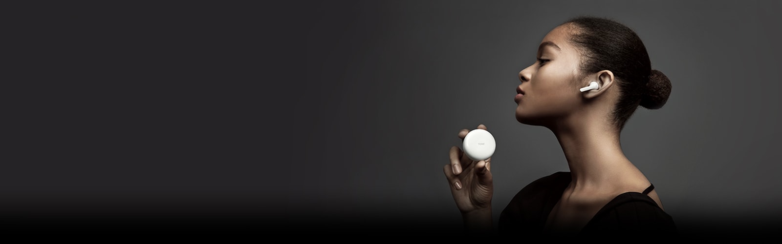 Side view of woman holding LG TONE Free against a dark background.