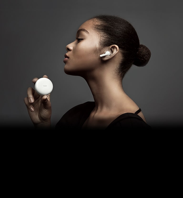 Side view of woman holding LG TONE Free against a dark background.
