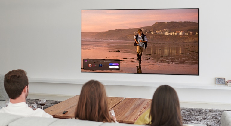 Three people watching TV screen showing a scene from a fantasy movie with a Sports Alert