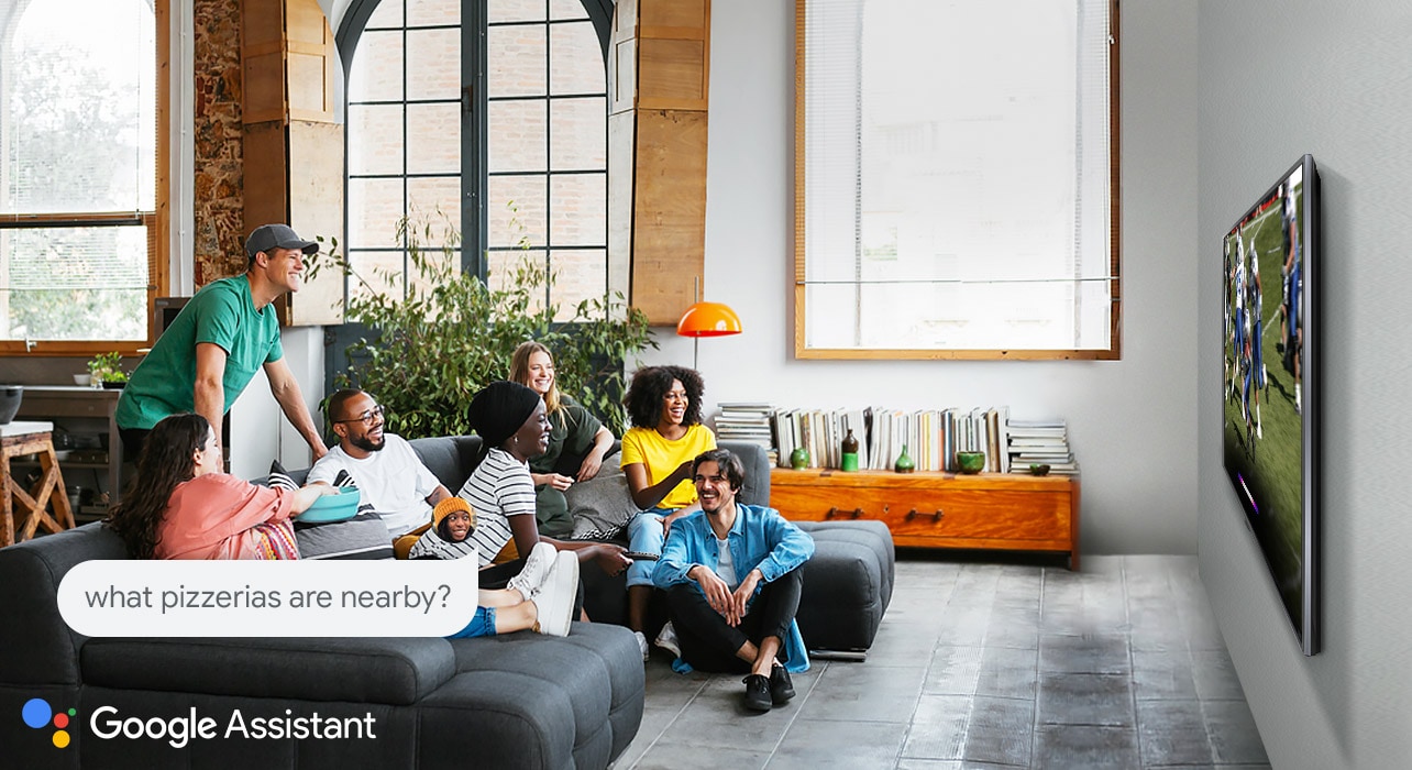 Woman watching football on TV with friends and asking the Google Assistant what pizzerias are nearby