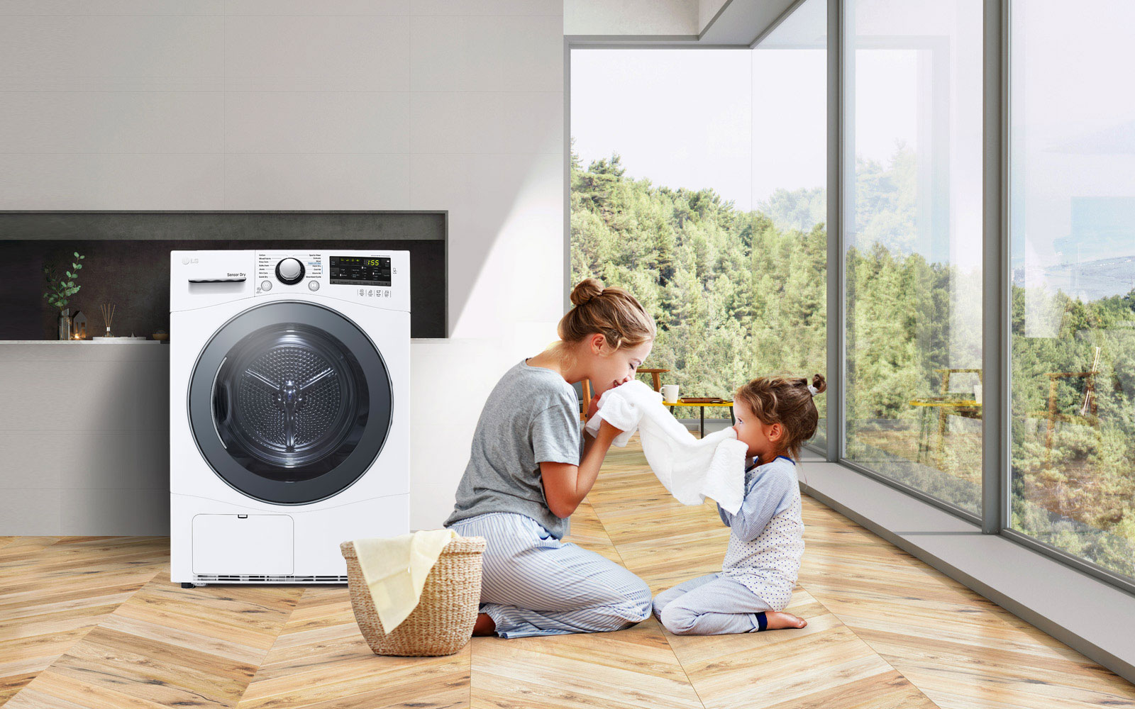 A mother and daughter sit on the floor holding and enjoying the smell of a towel that just came out of the Condensing Type Dryer that sits next to them.