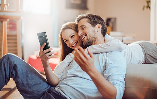 The couple is hugging each other and smiling while looking at the smartphone.