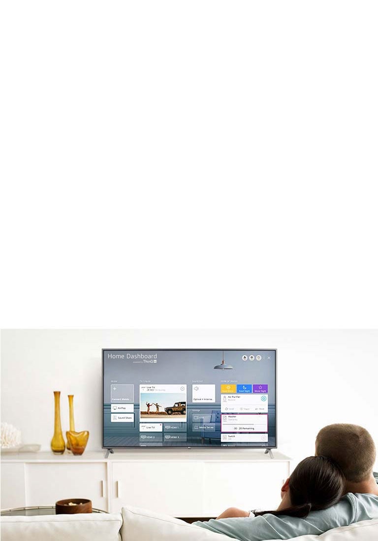 A men and women sitting on a sofa in the living room with the Home Dashboard on the TV screen.