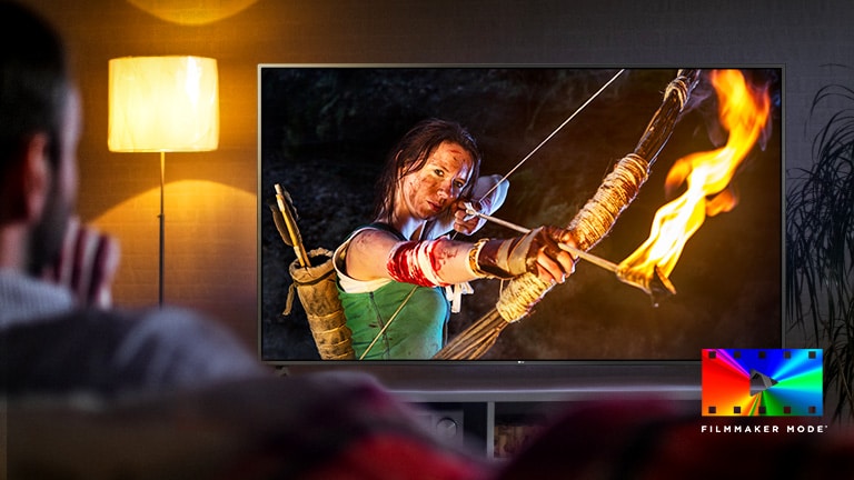 A man is sitting on a couch watching an action movie. The girl on the TV has a fully drawn bow and arrow.